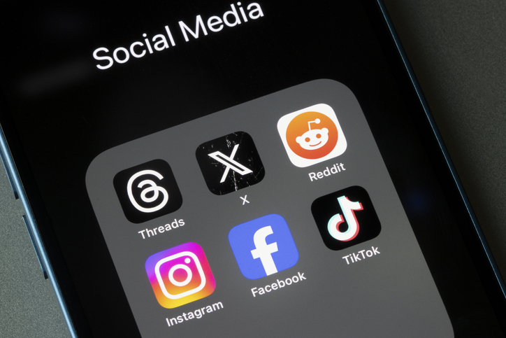 Smartphone screen displaying Threads, X, and other social media apps with active posts, notifications, engagement metrics, and content feeds, representing social media marketing and cross-platform audience engagement.