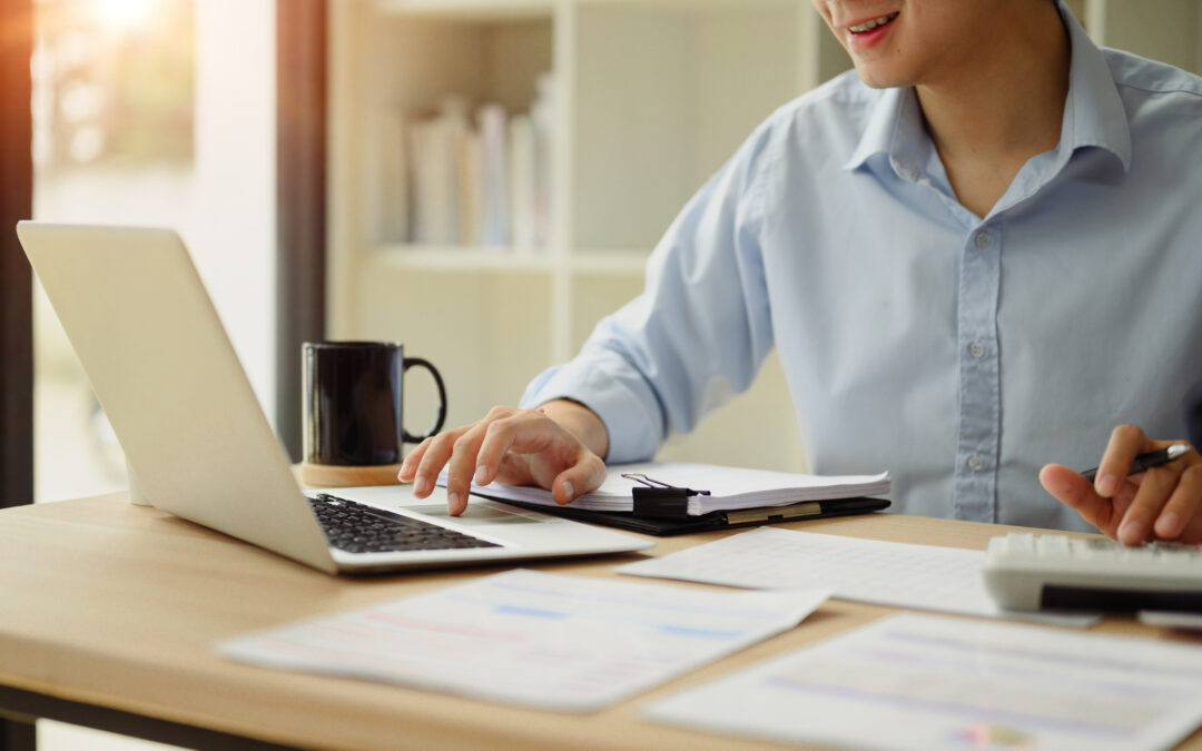 Close up of a businessperson using a calculator and laptop to budget for marketing for their small business.