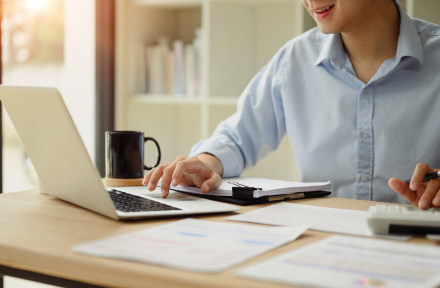 Close up of a businessperson using a calculator and laptop to budget for marketing for their small business.