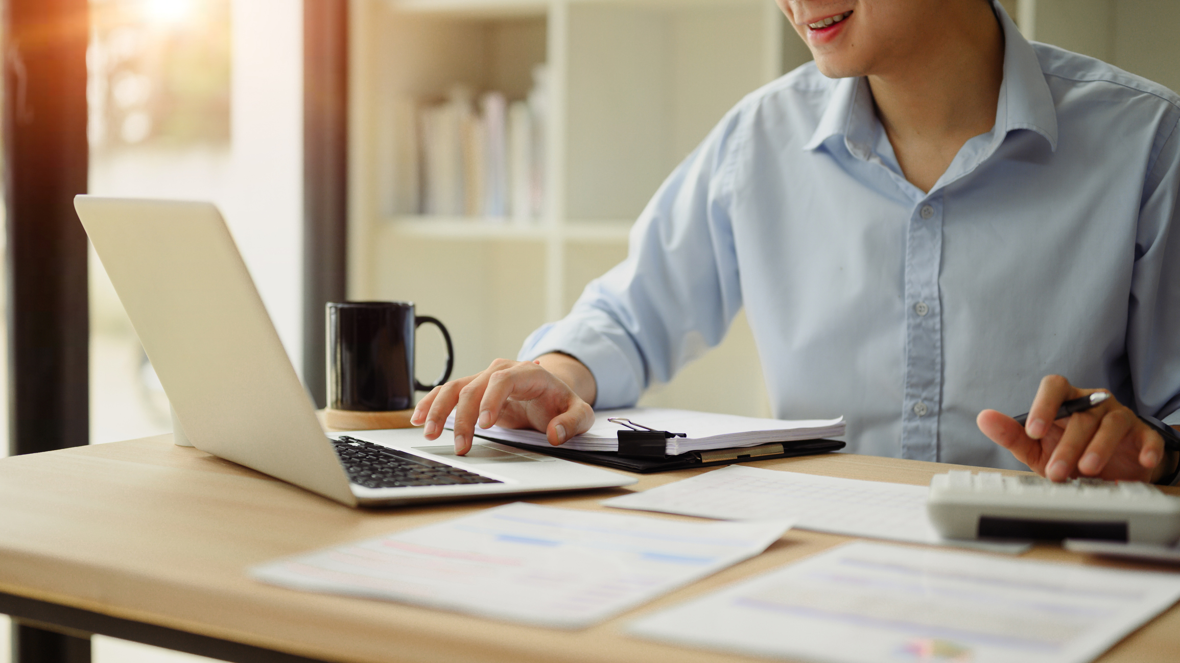 Close up of a businessperson using a calculator and laptop to budget for marketing for their small business.